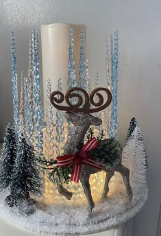 a lit candle with reindeer and trees on it in front of a frosted wall