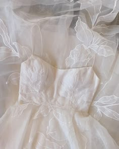 a white dress with flowers on it is laying on a bed sheet and has sheer fabric