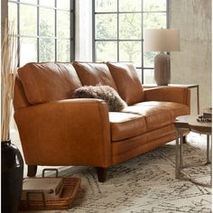 a brown leather couch sitting on top of a rug next to a table with a lamp