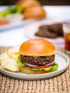 a hamburger with lettuce, onion and tomato on a plate next to chips