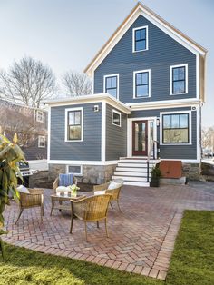 a blue house with white trim on the front and side windows, sitting in grass next to a brick patio