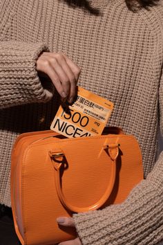 a woman holding an orange purse with a card in her hand and a tag on it