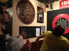 two men are standing in front of darts on the wall and pointing at them