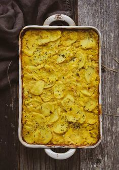 a casserole dish with potatoes and herbs in it sitting on a wooden table