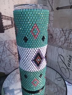 a green and white beaded cup sitting on top of a glass table