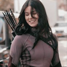 a woman with long black hair is holding an arrow in her hand and smiling at the camera