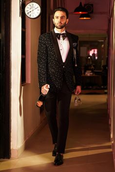 a man in a tuxedo and bow tie walking down a hallway with a clock on the wall