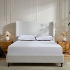 a bed with white sheets and pillows in a room next to two nightstands on either side of the bed