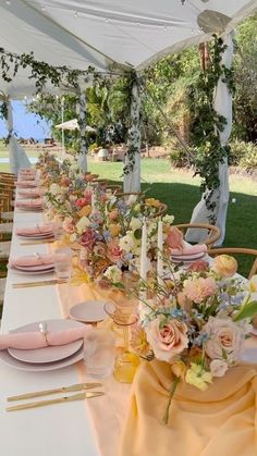 a long table is set with pink and yellow plates, napkins, and flowers