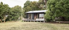 a small cabin in the middle of a field with trees and grass around it,