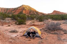 two men are sitting in front of a tent on the side of a dirt road