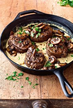 some meat and mushrooms are in a skillet on a wooden table with parsley