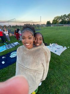 two young women are posing for a photo on the grass in front of a soccer field