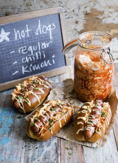 three hot dogs with condiments in front of a chalkboard