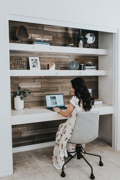 a woman sitting at a desk with a laptop computer in front of shelving unit