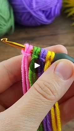 a person holding a crochet hook in their left hand and several balls of yarn on the other