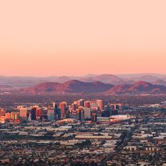 an aerial view of a city with mountains in the back ground and pink sky above