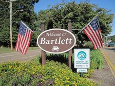 a welcome sign to the town of barlett with american flags hanging from it's sides