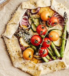 a pizza topped with lots of veggies on top of a piece of parchment paper