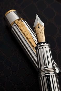 a fountain pen sitting on top of a black cloth covered table next to a gold and silver object