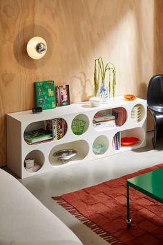 a white shelf with books and magazines on it next to a chair in a living room