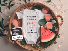 a baby's bodysuit, watermelon and roses are on display in a basket