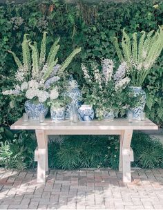 blue and white vases sitting on top of a wooden table next to green plants