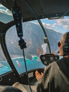 two people in the cockpit of an airplane looking out at mountains and blue water below