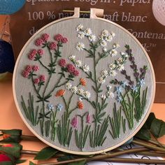 an embroidery kit with flowers on it sitting next to some knitting needles and yarn balls