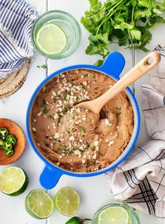 a blue pot filled with mexican style hummus next to limes and cilantro