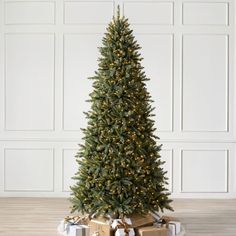 a christmas tree with presents under it on a wooden floor in front of a white wall