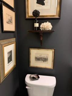 a white toilet sitting in a bathroom next to pictures on the wall and framed artwork