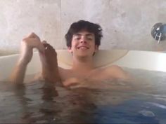 a young man is in the bathtub with his hands up and smiling at the camera