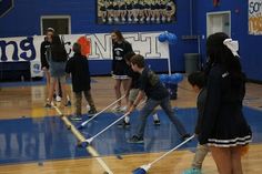 several young people are playing with brooms in a gym