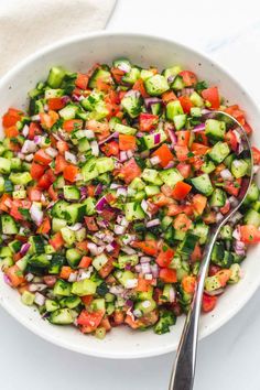 a white bowl filled with cucumber, red onion and tomato salad next to a spoon