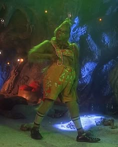 a man dressed in green and yellow is standing next to a cave with lights on