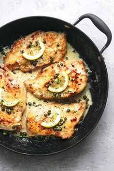 chicken with lemons and capers in a skillet on a white table top