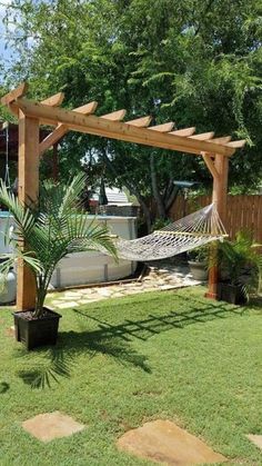 an outdoor hammock in the middle of a yard with a tree and potted plant