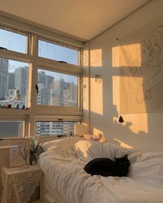 a black cat laying on top of a white bed in a room with large windows