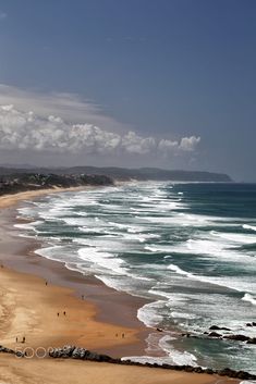 people are walking on the beach next to the water and sand, with waves coming in from the ocean