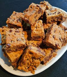 a white plate topped with lots of brownies and chocolate chip bars on top of a table