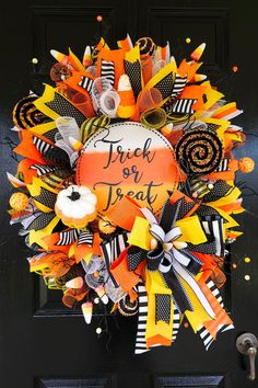 an orange and black halloween wreath on a door with the words trick or treat written on it