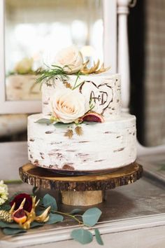 a white wedding cake with flowers on top sitting on a table next to a mirror