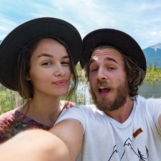 a man and woman taking a selfie in front of a lake with mountains behind them