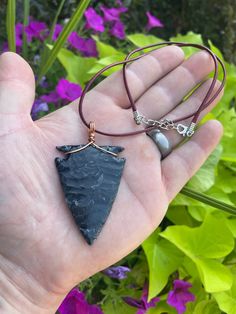 a hand holding a piece of black stone in it's palm with purple flowers behind it