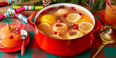 a red pot filled with fruit and topped with lemons next to two glasses of orange juice