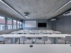 an empty classroom with white desks and chairs in front of a projector screen