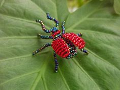 a red and blue beaded bug sitting on top of a green leaf covered in beads