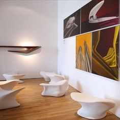 white chairs are lined up against the wall in a room with wood floors and artwork on the walls