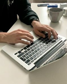 a person using a laptop computer on a white table with cups and saucers in the background